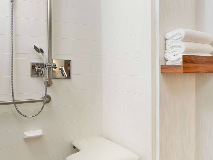 Un baño moderno con ducha a nivel, inodoro con barra de apoyo y estante con toallas dobladas.