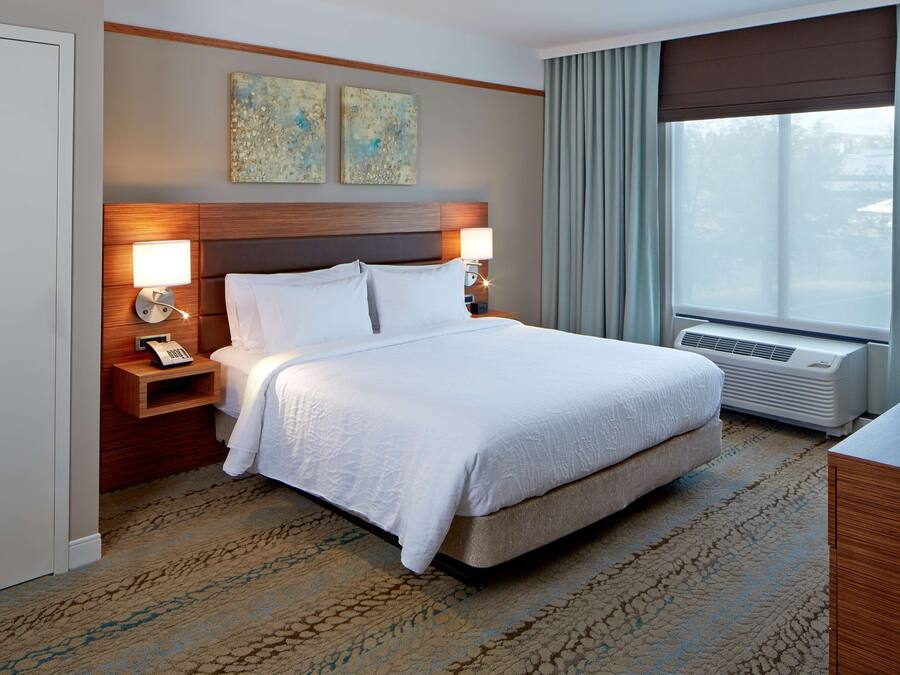 A hotel room with a large bed, two bedside lamps, a telephone, and a television.