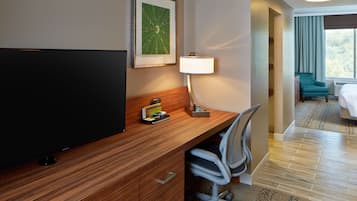 Een hotelkamer met een houten bureau, een televisie, een lamp, een stoel en een bed.