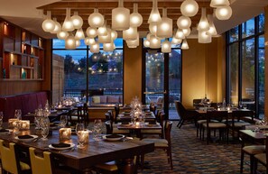 Un restaurant doté de nombreuses tables, de grandes fenêtres donnant sur l’extérieur et d’une variété de luminaires suspendus.