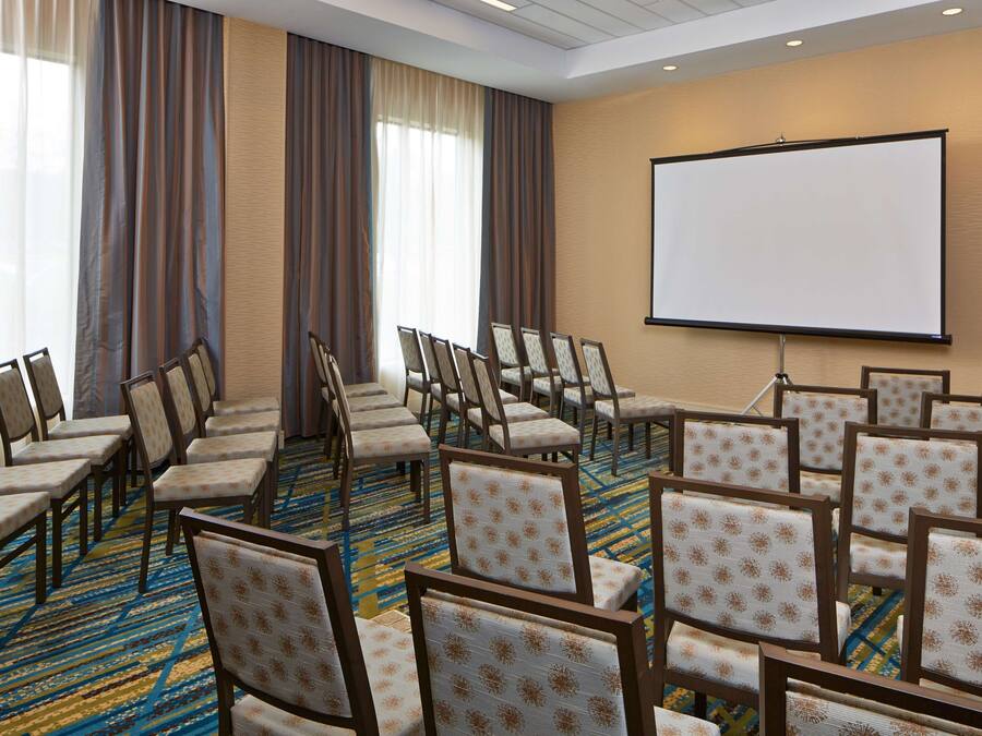 Un salón de conferencias con filas de sillas, una pantalla de proyección grande y una alfombra estampada.