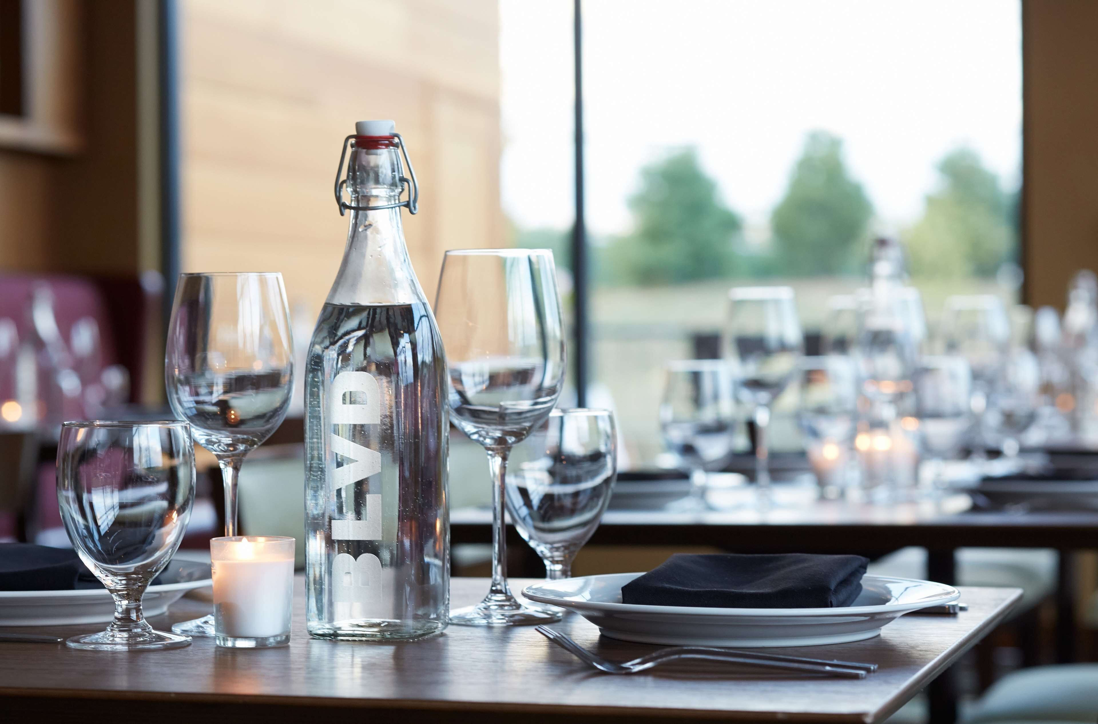 A dining table set with wine glasses, a candle, and a bottle of water.