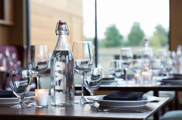 Une table à manger dressée avec des verres à vin, une bougie et une bouteille d’eau.