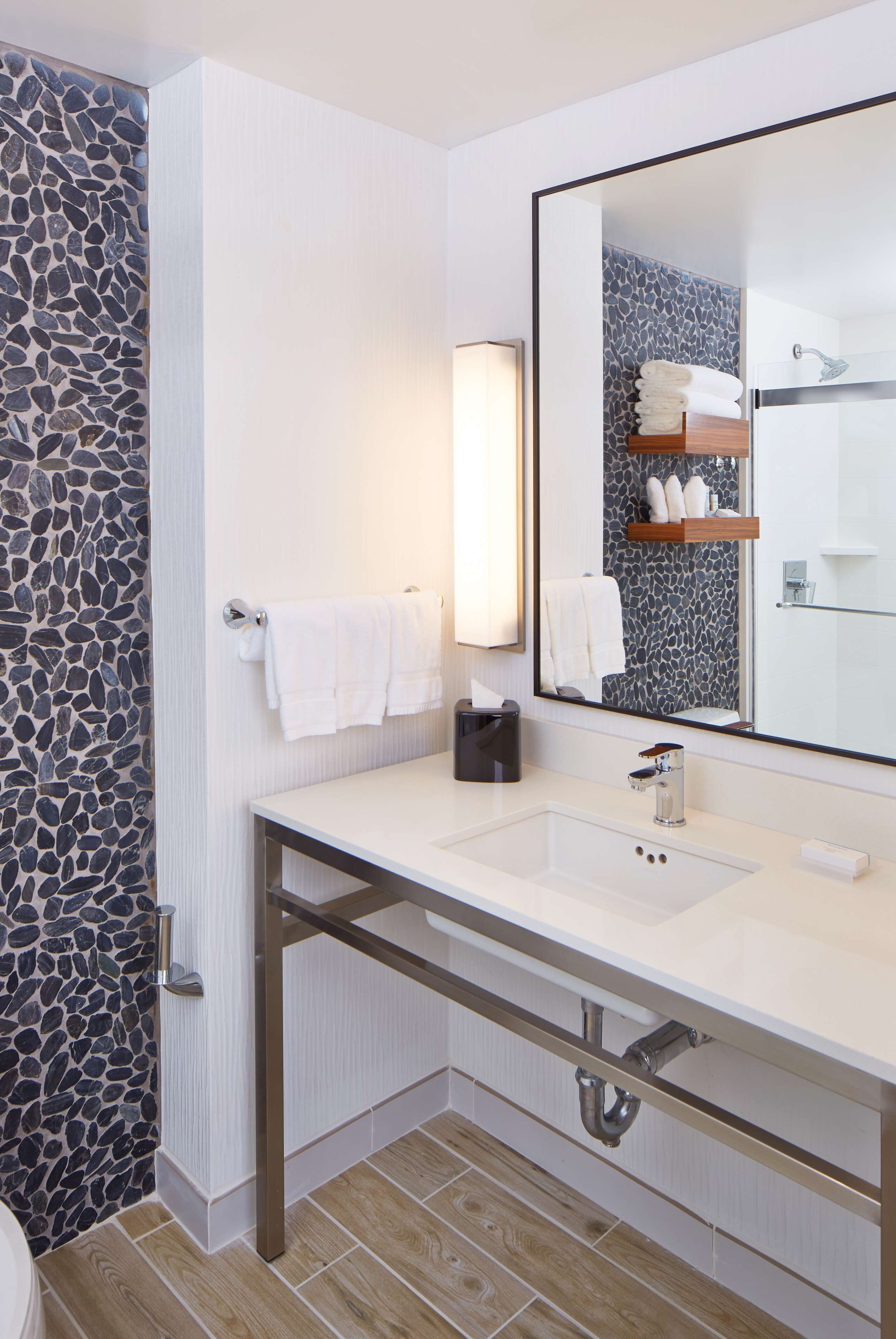Un baño con pared de piedra, un lavabo blanco, un espejo y un perchero para toallas.
