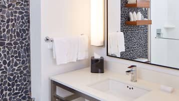 Un baño con pared de piedra, un lavabo blanco, un espejo y un perchero para toallas.