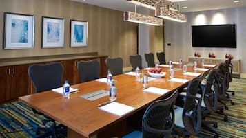 A conference room with a long table, chairs, water bottles, and a flat-screen TV on the wall.