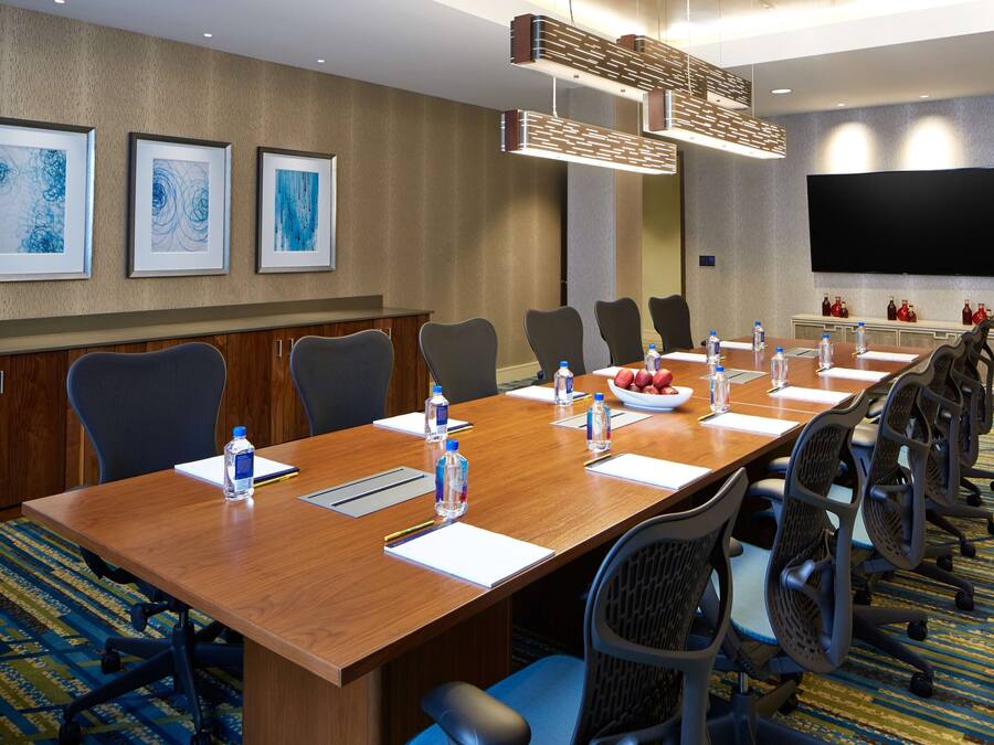 A conference room with a long table, chairs, water bottles, and a flat-screen TV on the wall.