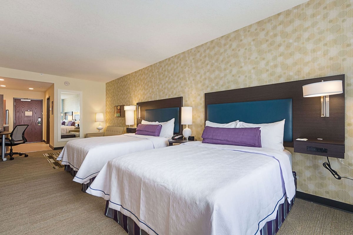 A hotel room with two beds, a desk, a chair, and a bathroom door.