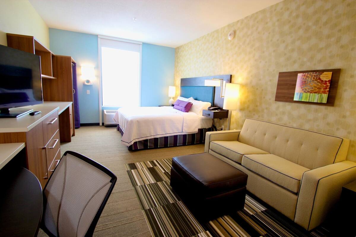 A hotel room with a bed, a sofa, a TV, a desk, and a chair.