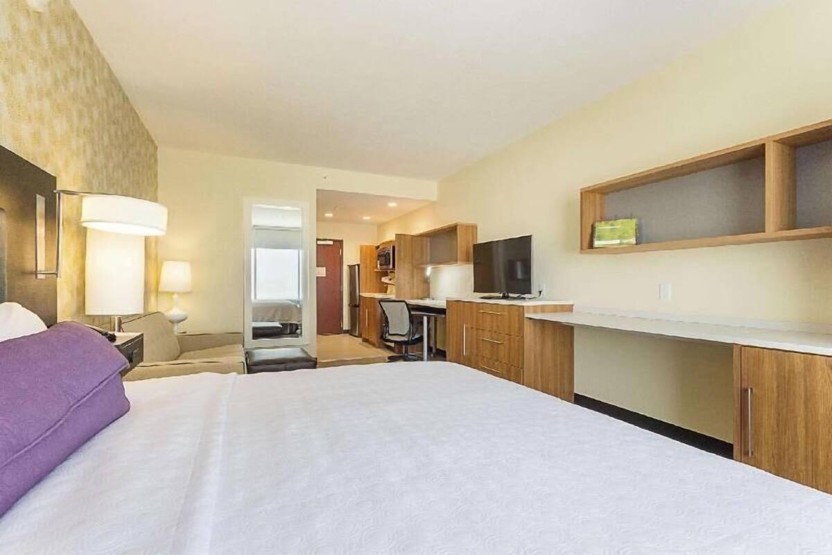 A hotel room with a bed, desk, TV, and a small kitchenette.