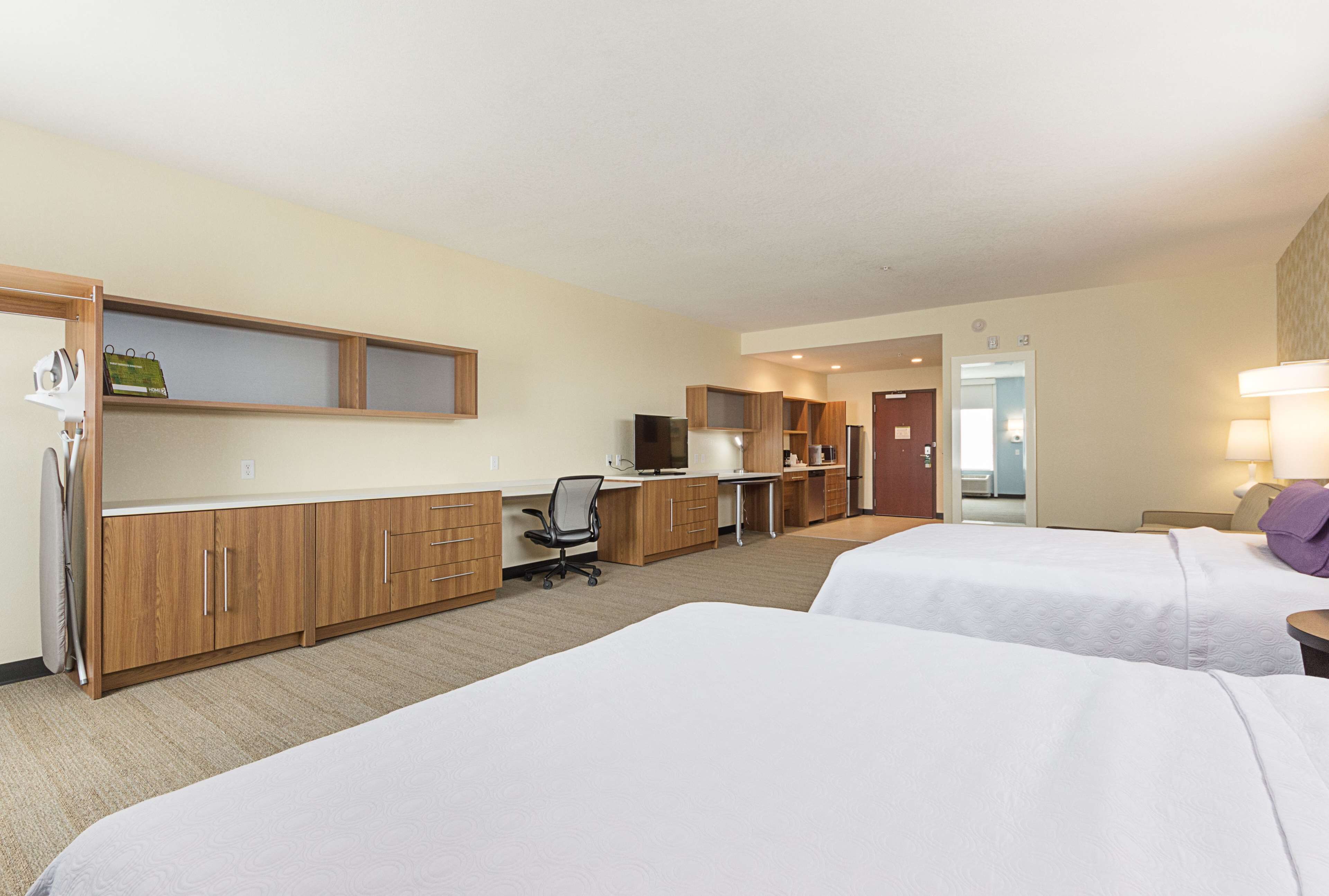 Une chambre d’hôtel avec deux lits, un bureau avec un ordinateur, une chaise et une kitchenette.