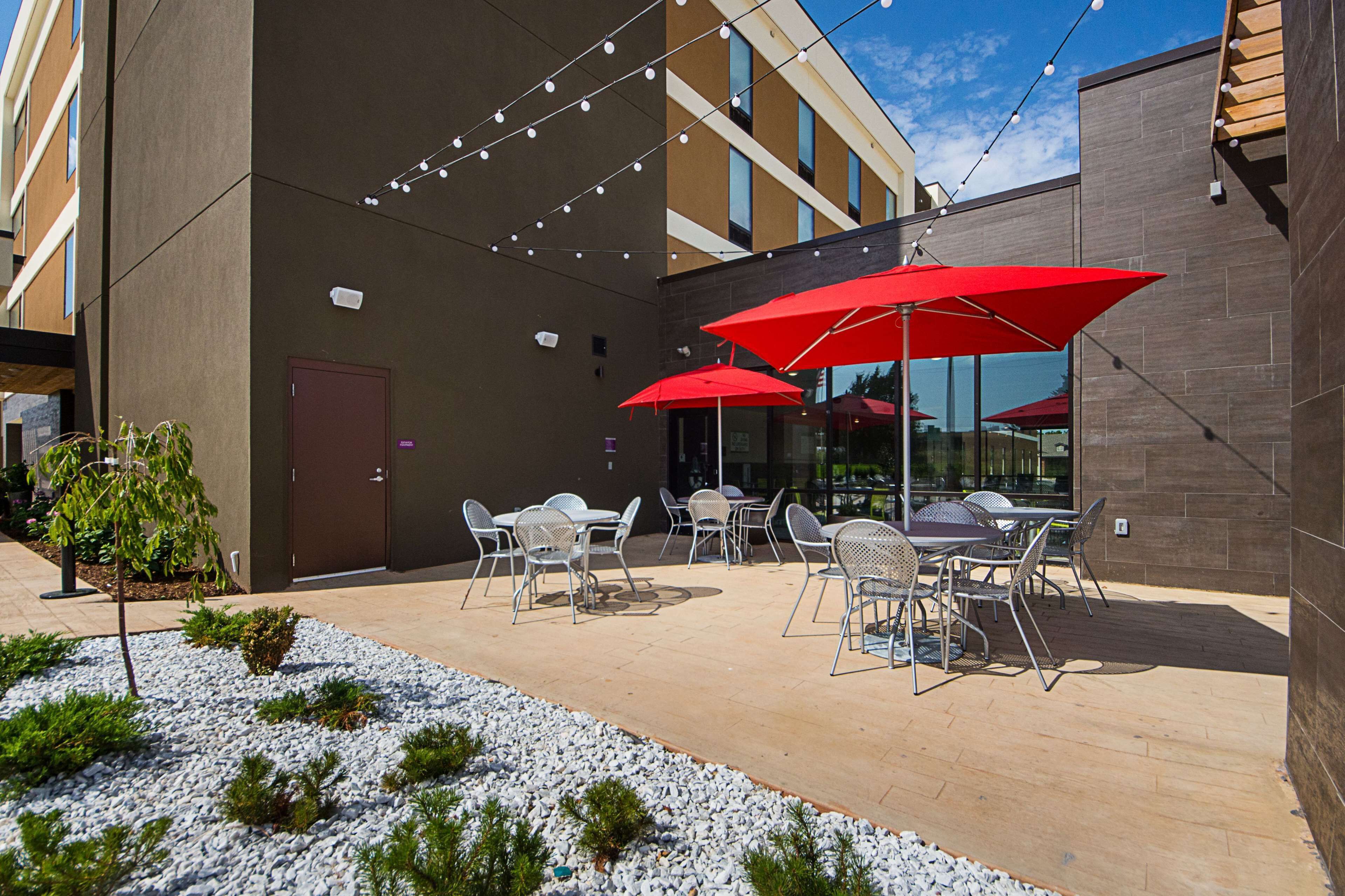 An outdoor patio area with tables and chairs, string lights, and red umbrellas.