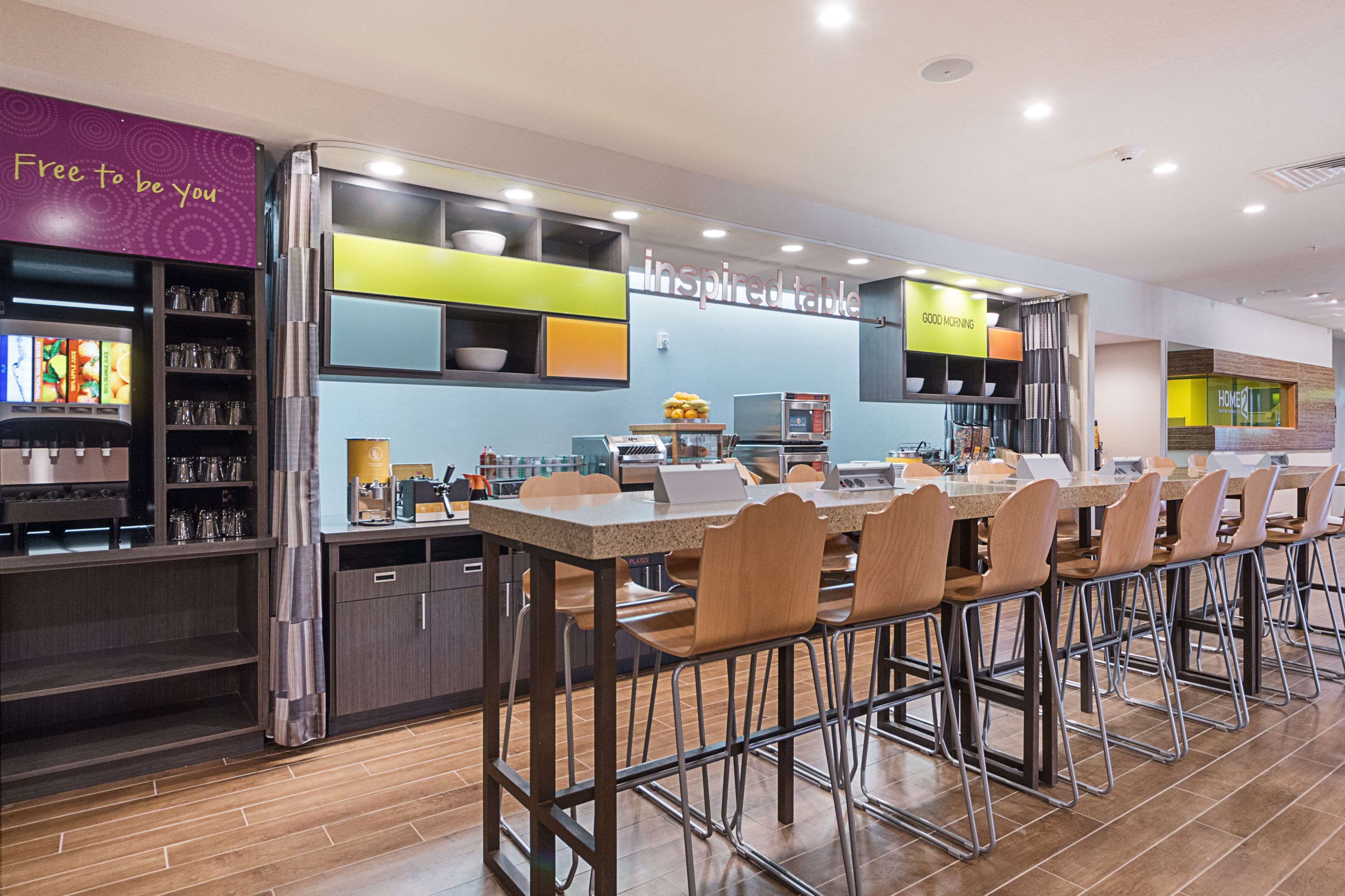 Un restaurante moderno con una barra alargada y varias sillas, una máquina de café y un panel con la carta.
