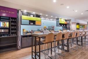 Un restaurante moderno con una barra alargada y varias sillas, una máquina de café y un panel con la carta.