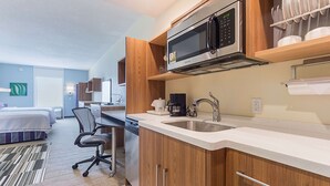 Een moderne keuken met een magnetron, koffiezetapparaat en wastafel. In de aangrenzende kamer bevindt zich een bed en een bureau.