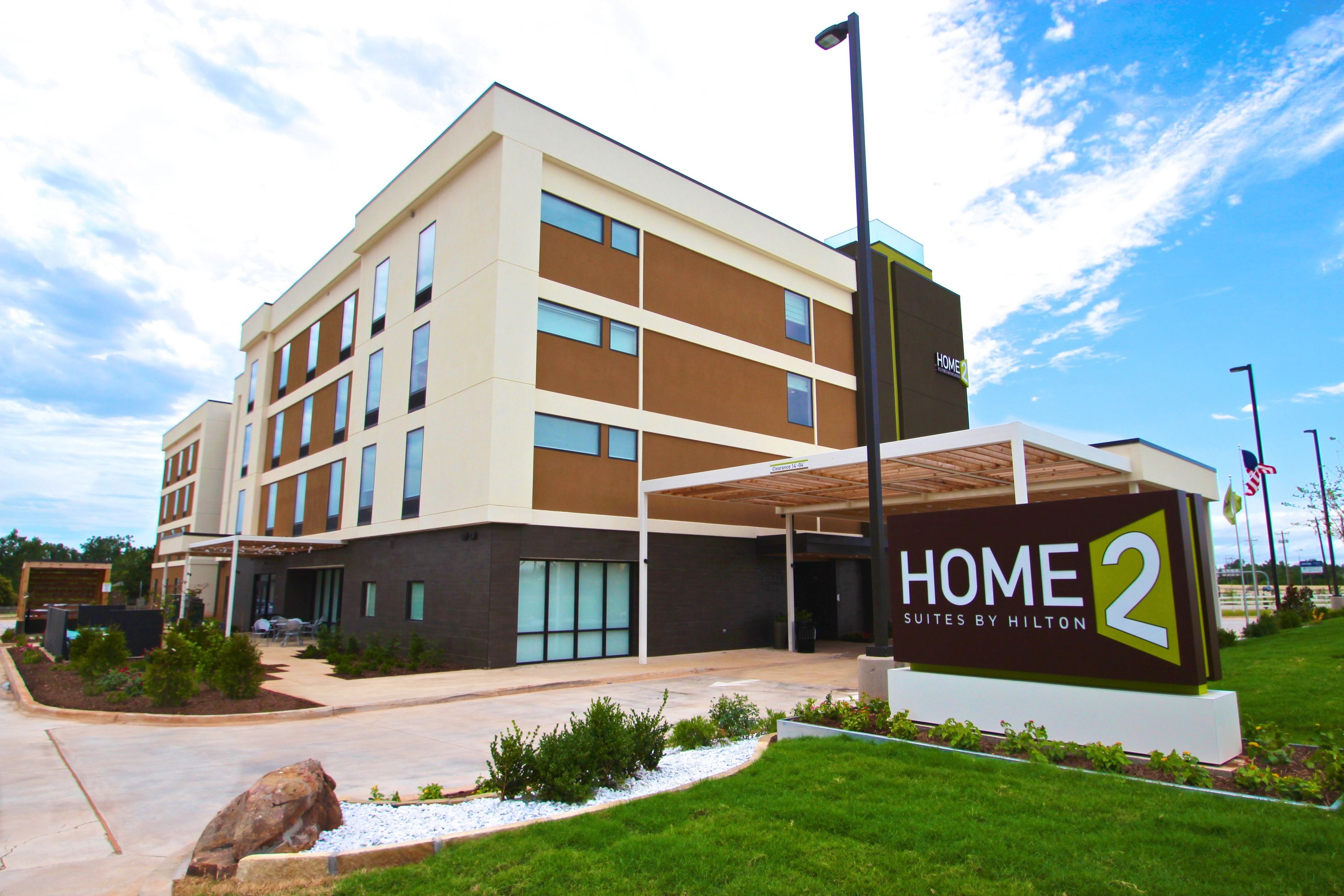 A multi-story hotel with a modern design, featuring a prominent sign for 'Home 2 Suites by Hilton'.