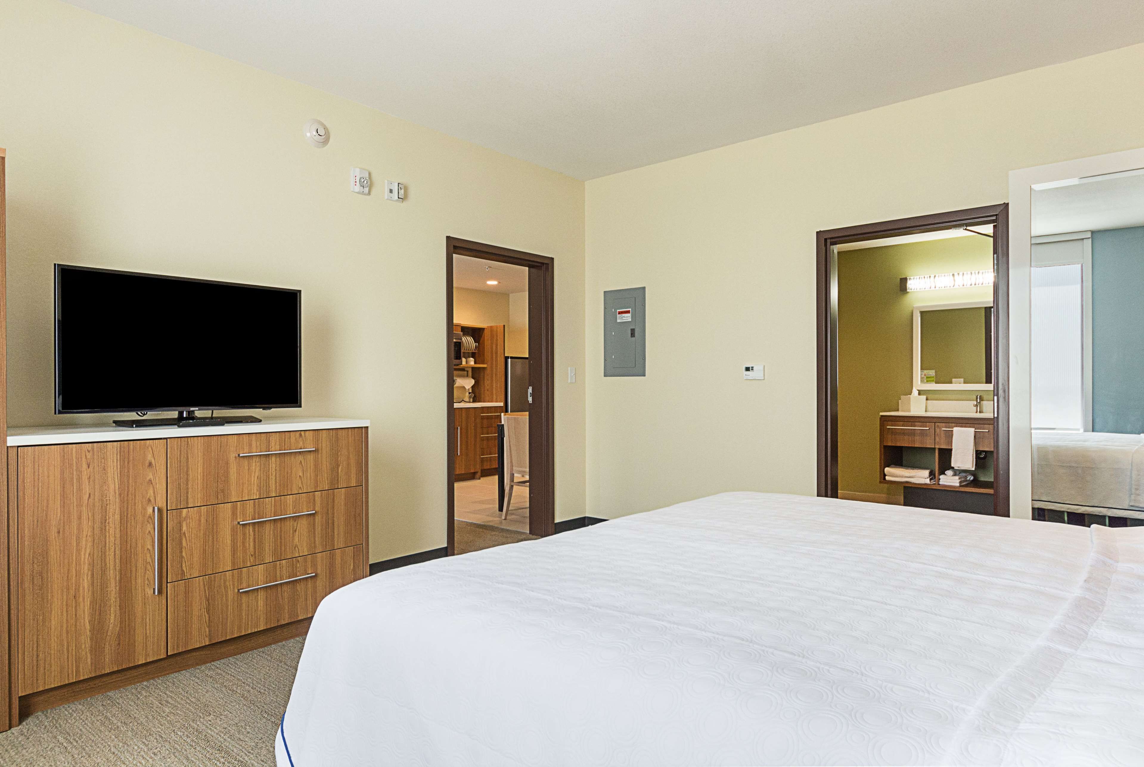 A hotel room with a bed, a TV on a wooden dresser, a bathroom with a mirror, and a walk-in closet.