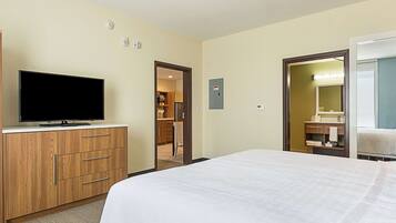 A hotel room with a bed, a TV on a wooden dresser, a bathroom with a mirror, and a walk-in closet.