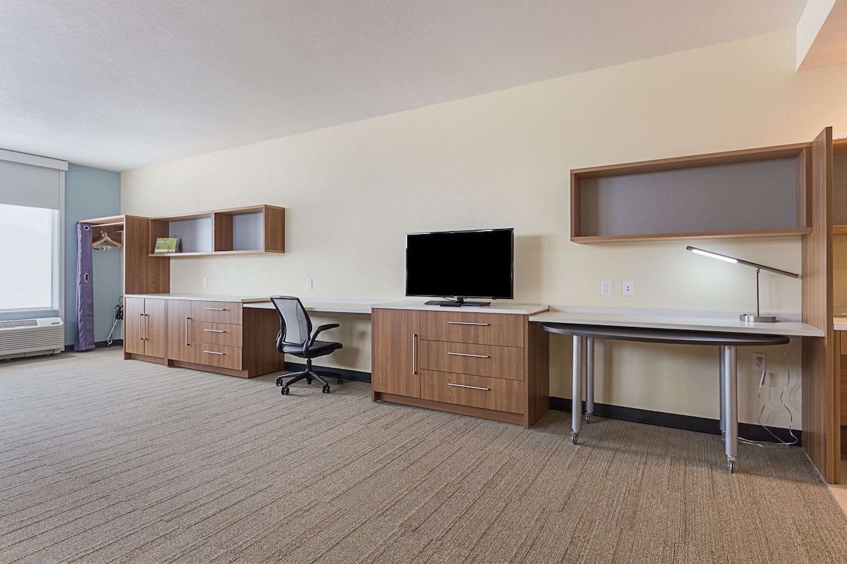 Une chambre d’hôtel équipée d’un bureau, d’une chaise, d’une télévision, d’une armoire et d’une grande fenêtre.