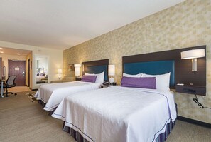 Habitación de hotel con dos camas, cada una con cabecero, lámparas de noche y suelo alfombrado.