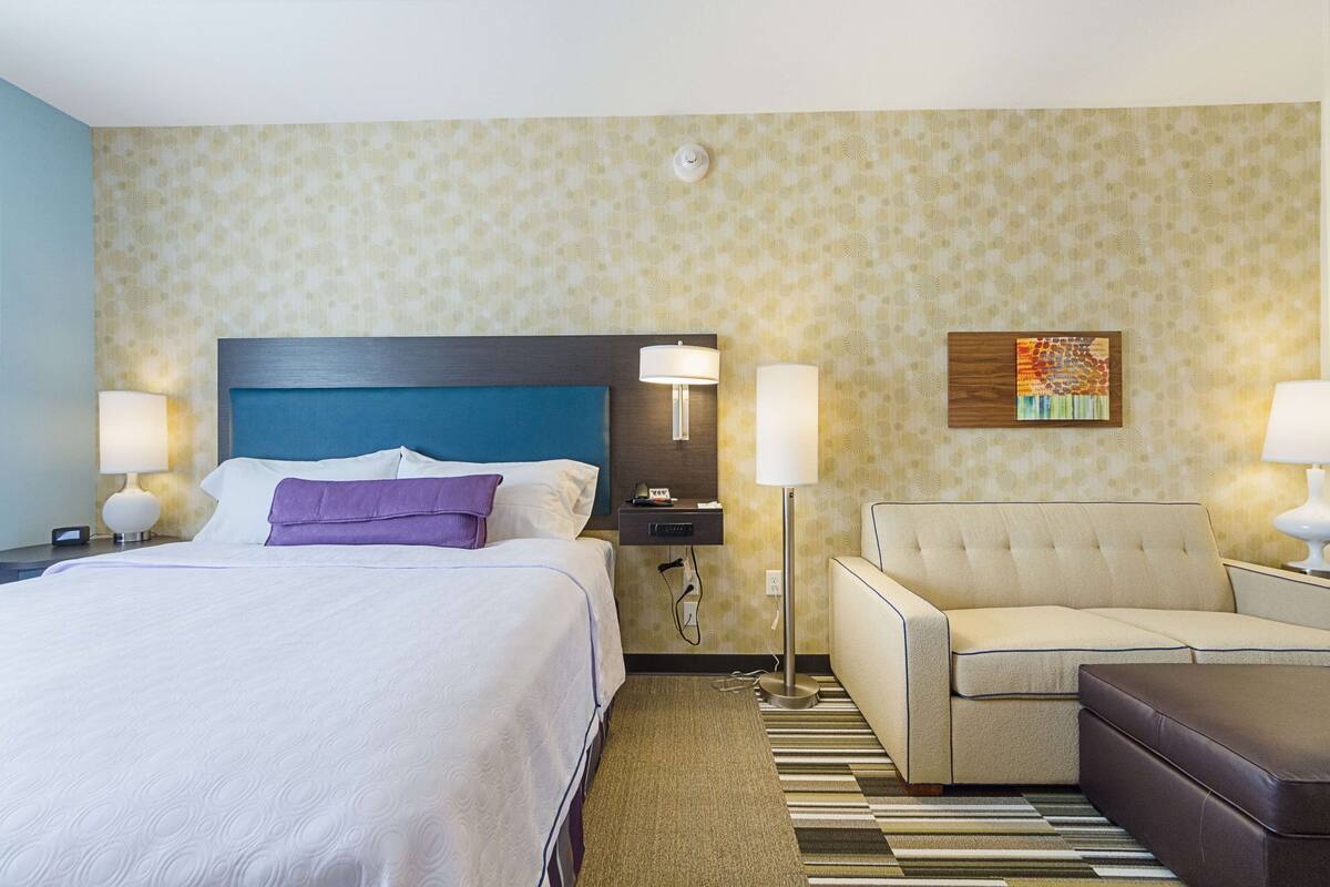 Une chambre d’hôtel avec un lit, un canapé, une petite table et une lampe.