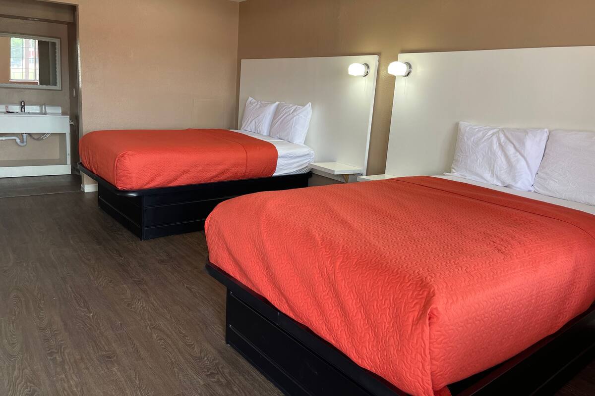 A hotel room with two beds, a bathroom, and a window.
