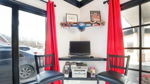 Una habitación con escritorio, dos sillas, una computadora portátil, una impresora y una ventana con cortinas rojas.