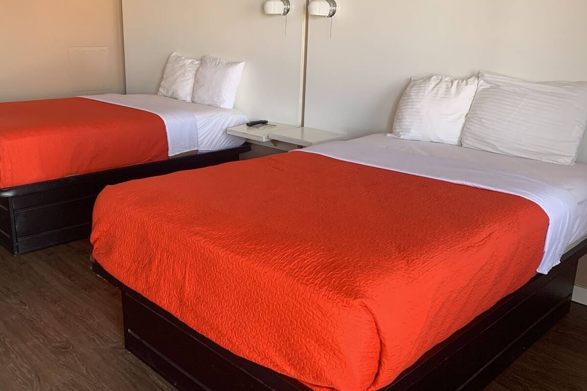 Two single beds with red and white bedding, wooden headboards, and a white wall with a light switch.