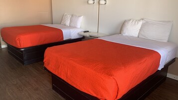 Two single beds with red and white bedding, wooden headboards, and a white wall with a light switch.