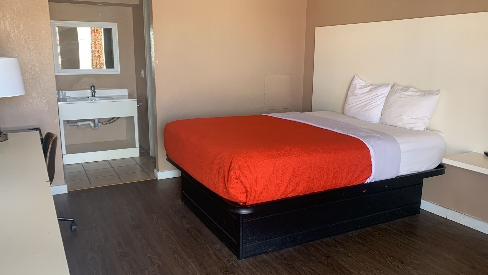 Un dormitorio con cama, mesita de noche, espejo y baño con lavabo e inodoro.