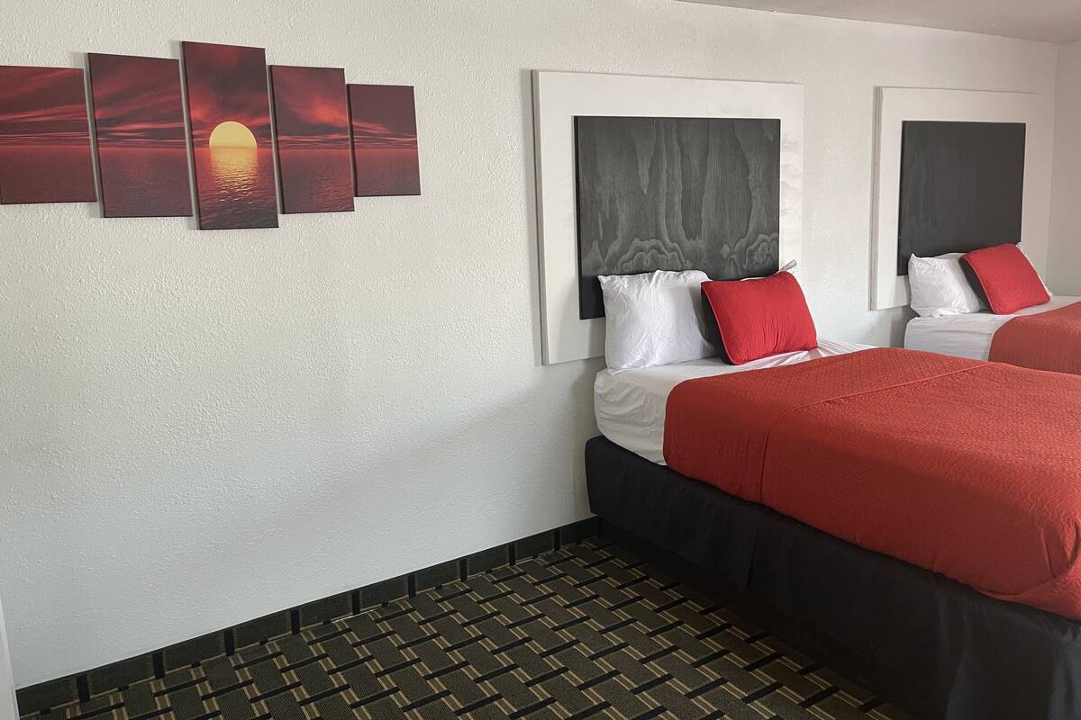 A hotel room with a bed, a headboard, a wall-mounted artwork, and a patterned carpet.