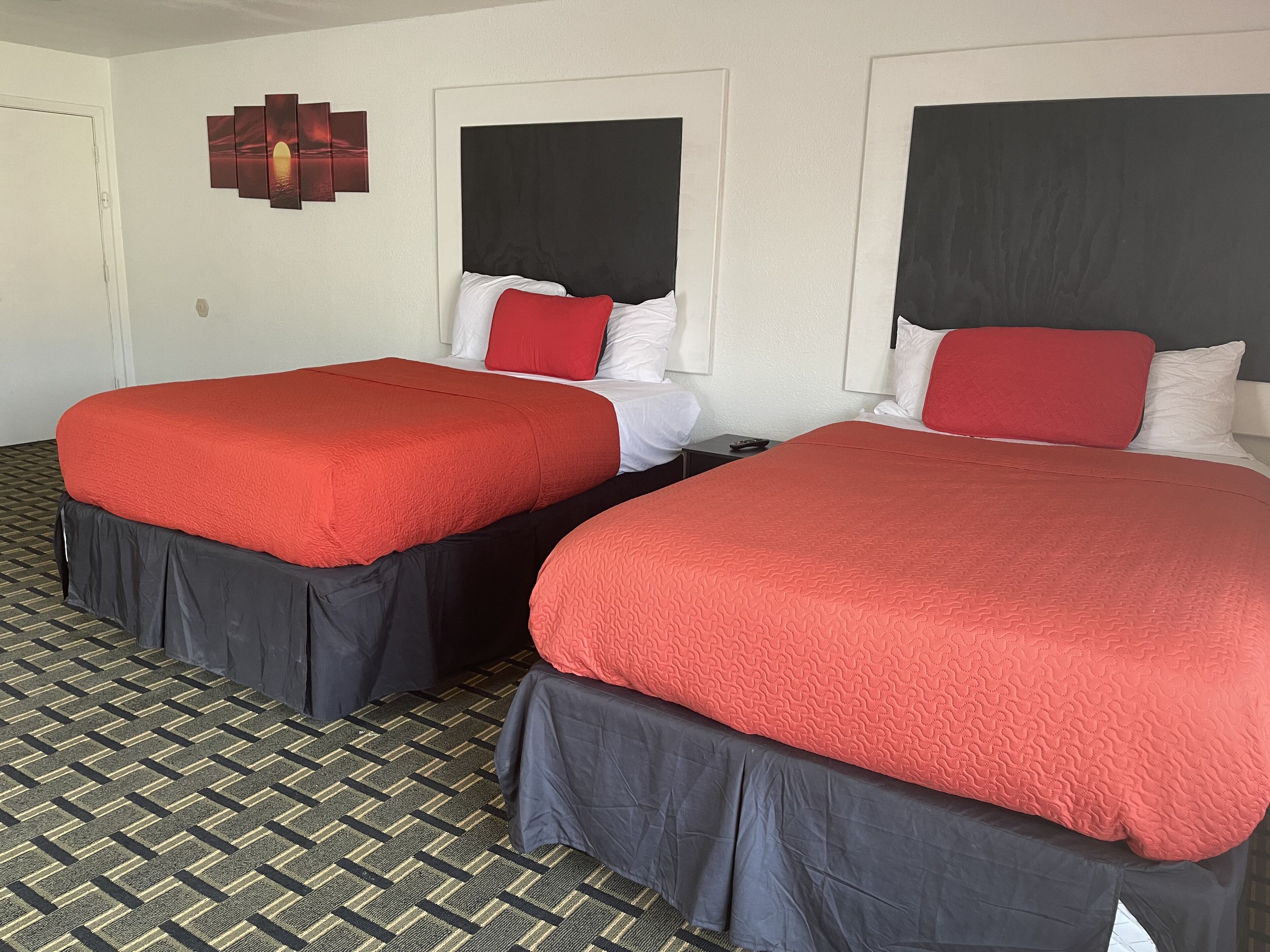 Two double beds with red and white bedding, a patterned floor, and a wall-mounted artwork.