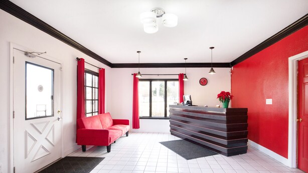 Un área de recepción con un sofá rojo, un mostrador de recepción y un amplio ventanal con cortinas rojas.