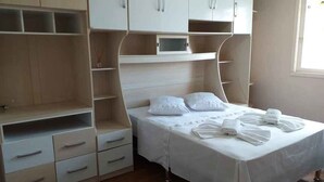 Une chambre à coucher avec un lit, des armoires blanches, une petite étagère et une fenêtre.