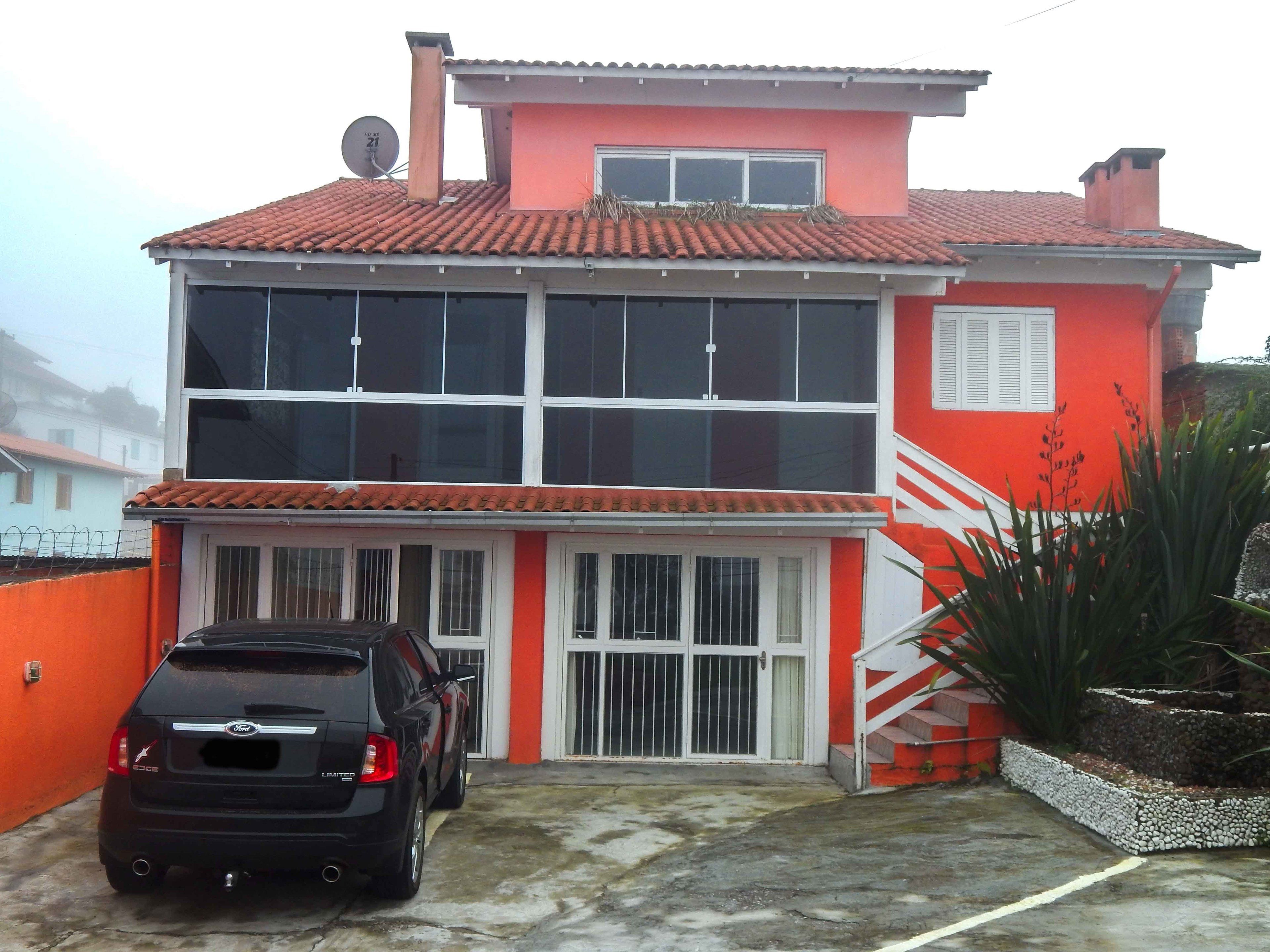 Una casa de dos pisos con fachada roja y blanca, un coche negro estacionado en frente y una antena parabólica en el techo.