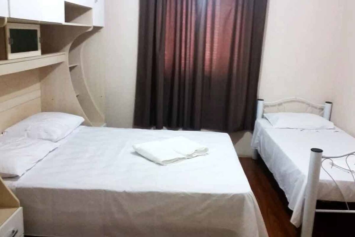 Une petite chambre avec deux lits simples, une étagère avec un téléviseur et un rideau.