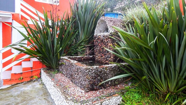 Un jardin agrémenté d’une fontaine en pierre, entouré de grandes plantes vertes.