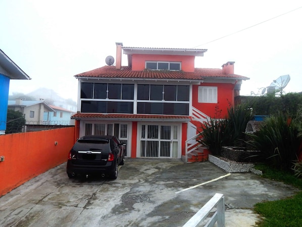 A two-story building with a red facade, a black car parked in front, and a satellite dish on the roof.