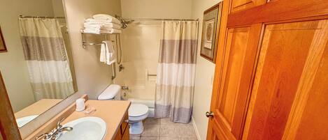A bathroom with a sink, toilet, shower, and wooden door.