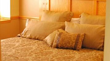 A neatly made bed with a patterned bedspread and several pillows, a bedside lamp, and a framed floral artwork on the wall.