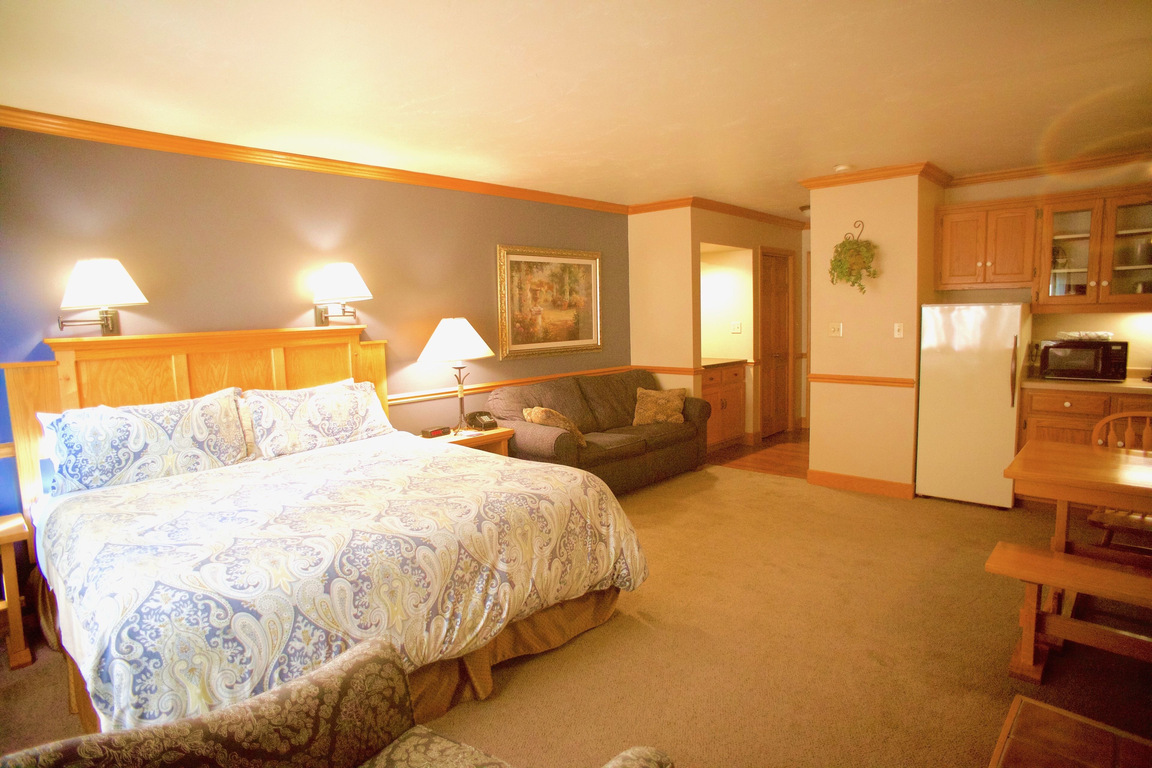 Un dormitorio con una cama grande, lámparas de noche, un sofá, una mesa de comedor y una zona de cocina con refrigerador y microondas.