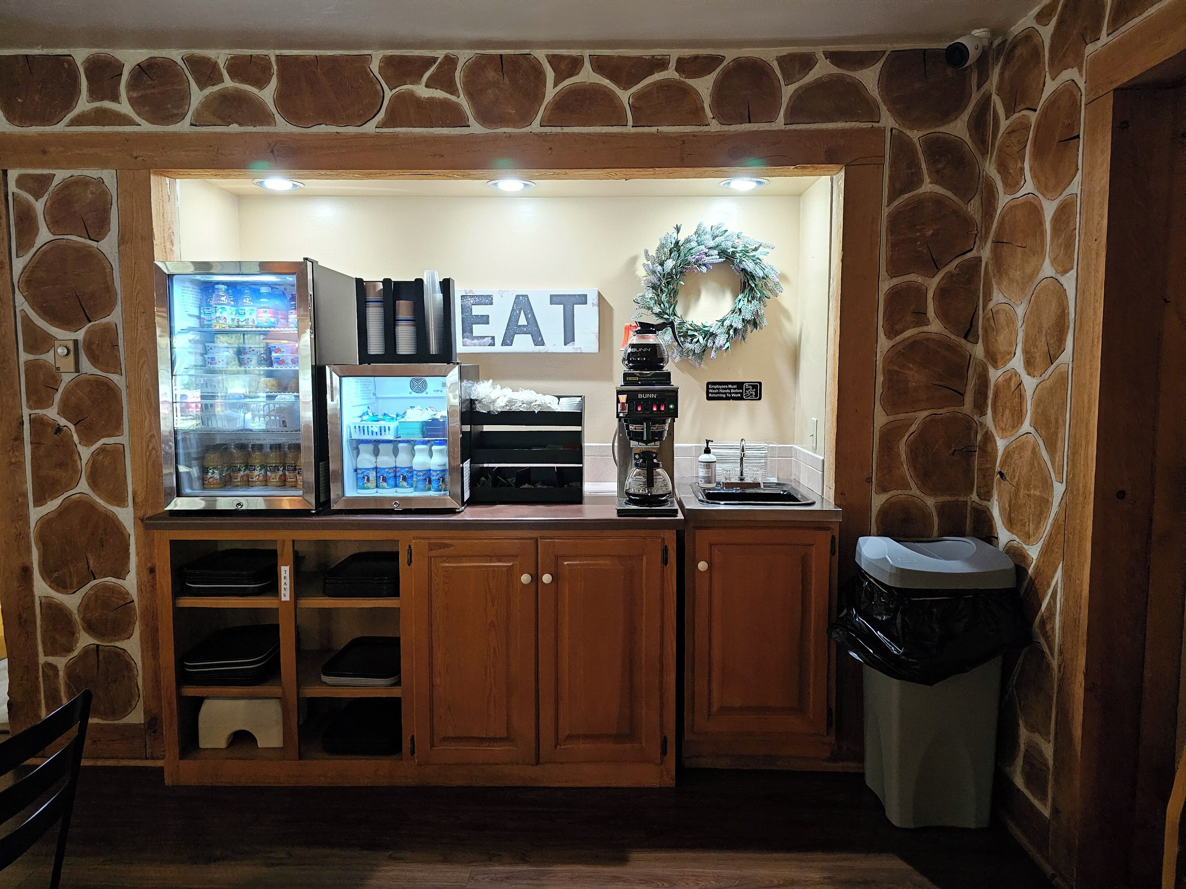 Una kitchenette con refrigerador, cafetera y un letrero que dice 'EAT'.