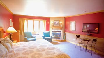 Une chambre d’hôtel dotée d’un grand lit, d’une cheminée, d’une télévision et d’un coin salon avec des fauteuils et une table.
