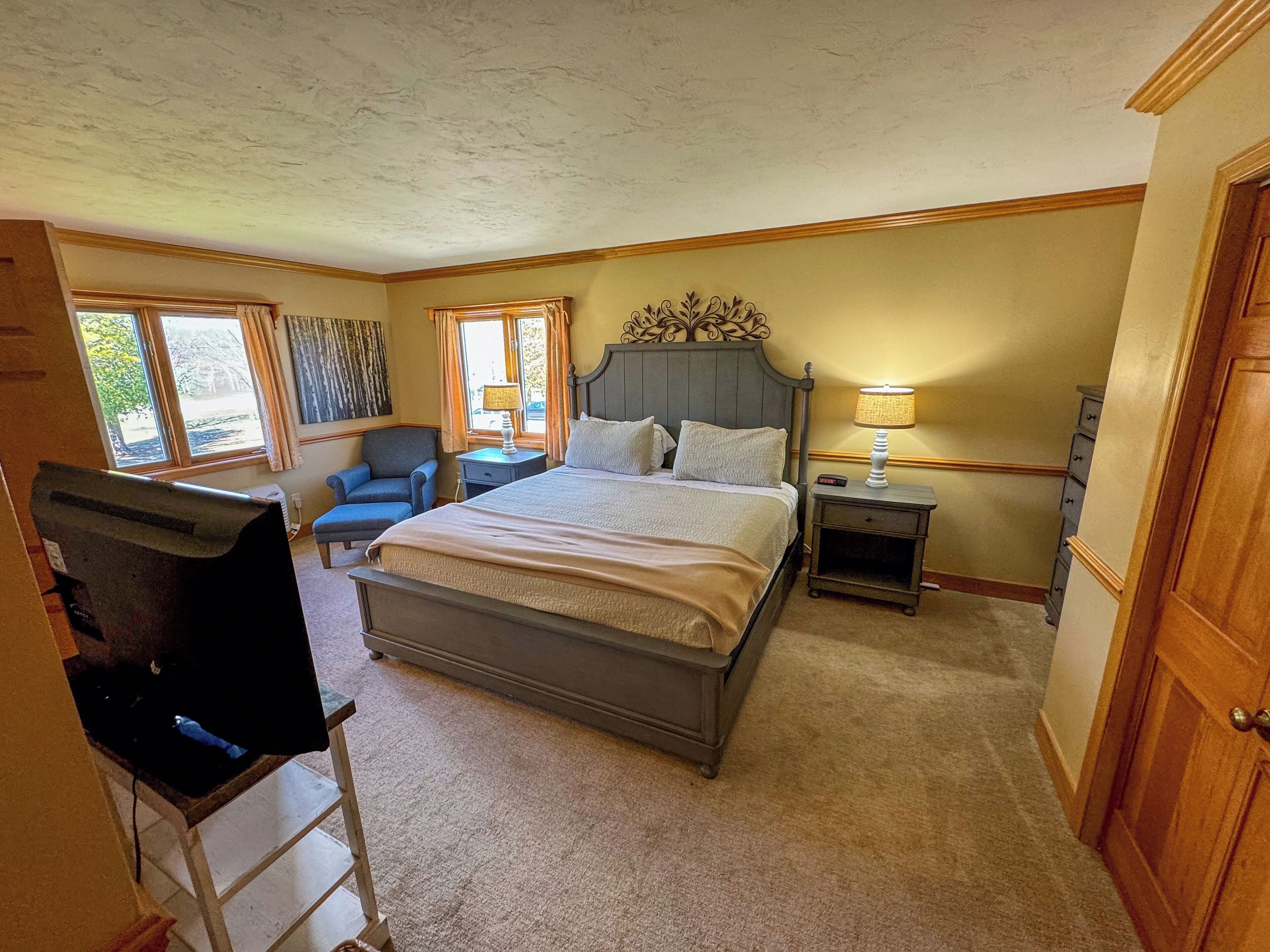A bedroom with a large bed, a chair, a desk, and a television.