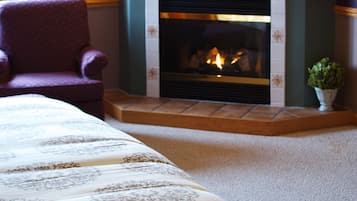 Una habitación de hotel con chimenea, una silla y una cama con colcha estampada.