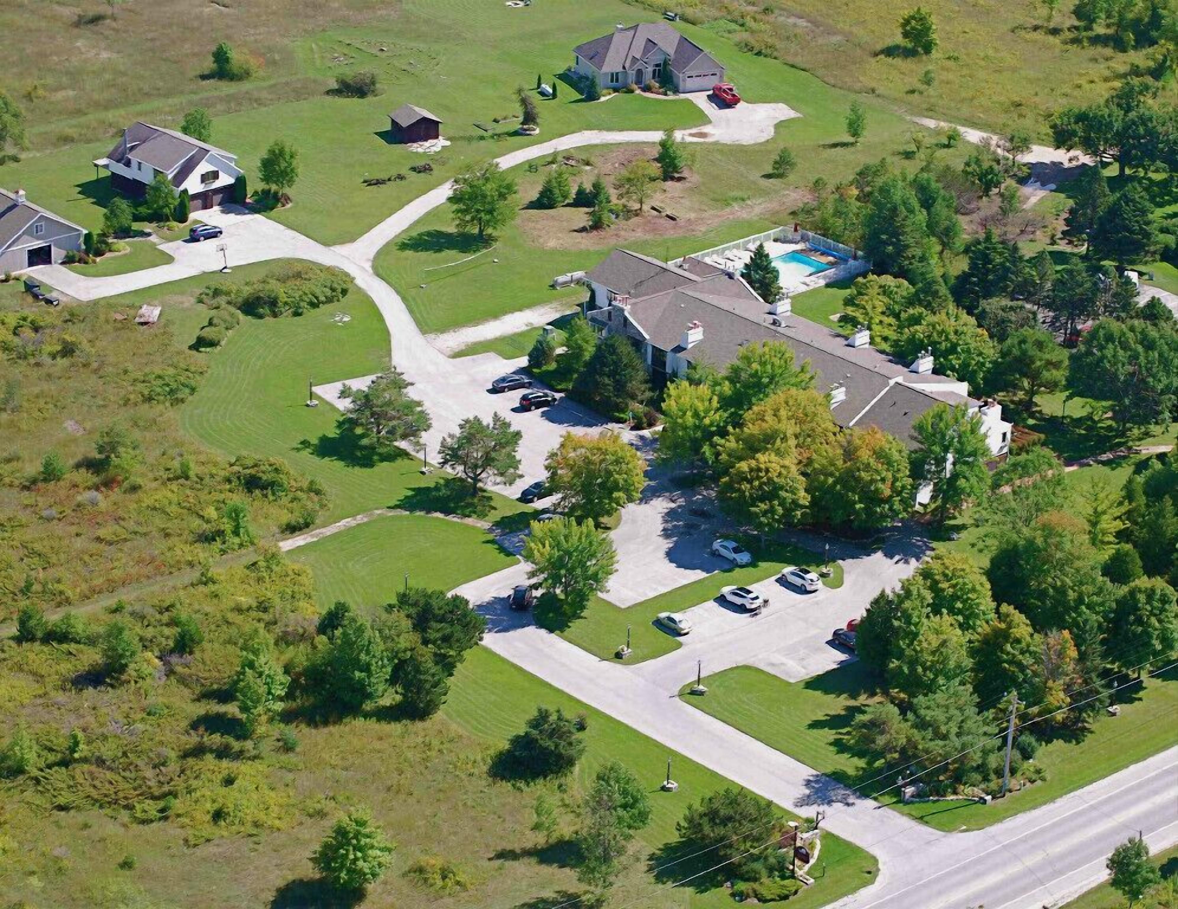 An aerial view of a residential area with multiple houses, a swimming pool, and a well-maintained lawn.