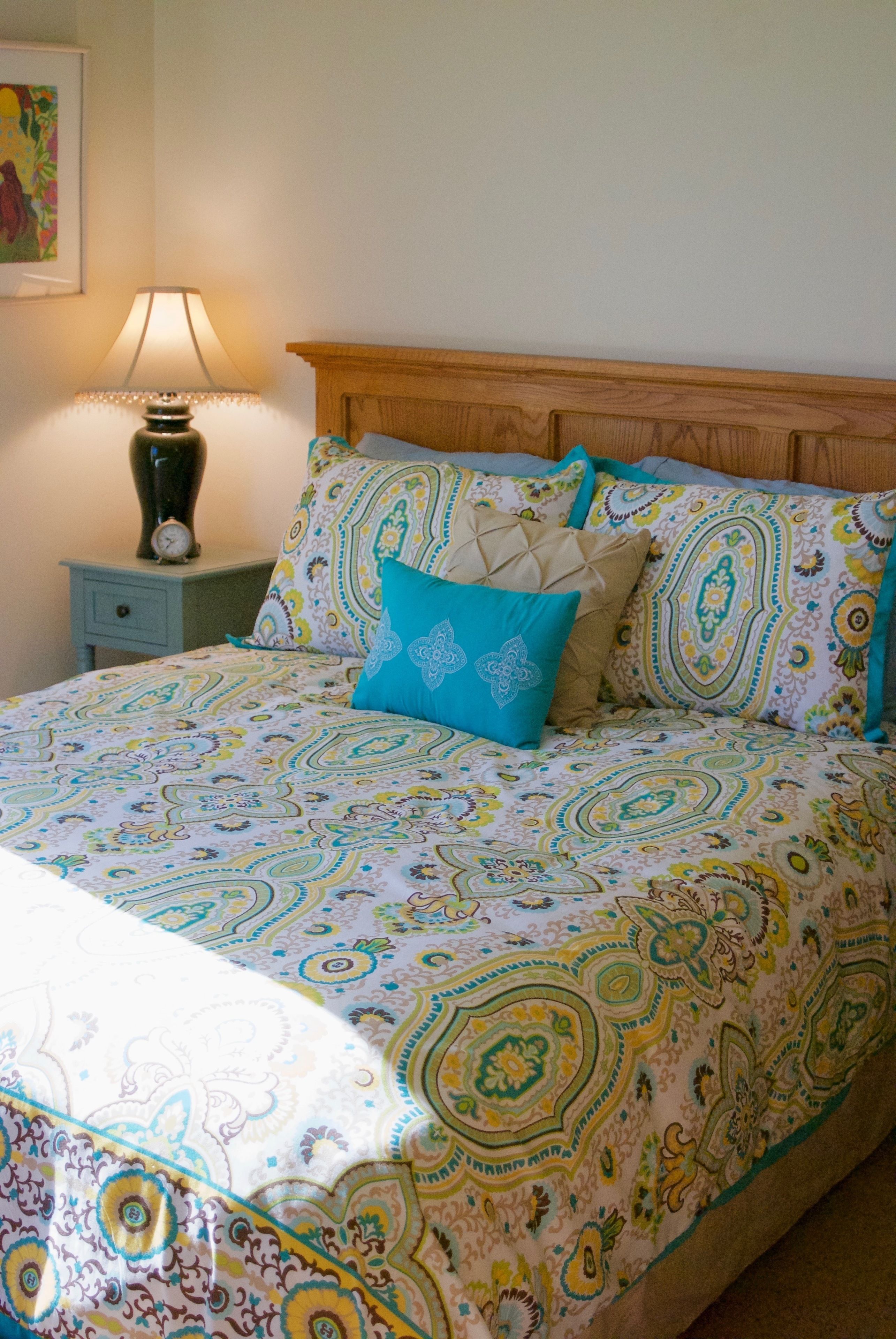 Una cama con colcha estampada, una mesita de noche con lámpara y un reloj de pared.