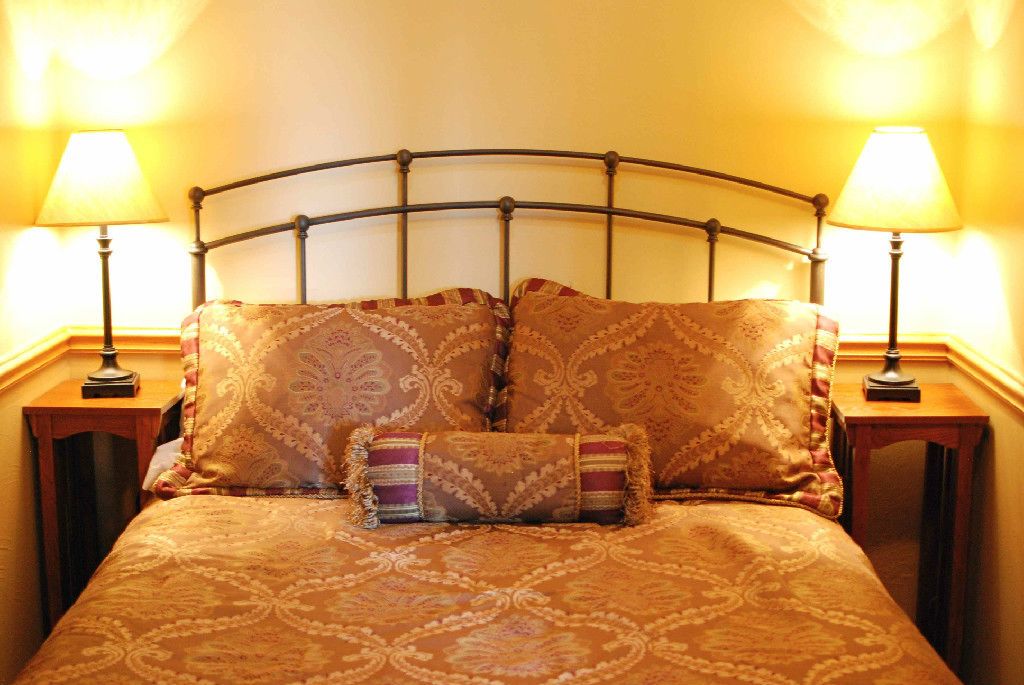 A bed with a metal headboard, two bedside lamps, and patterned bedding.