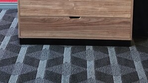 Ein TV-Schrank aus Holz mit einem Flachbildfernseher, zwei Schubladen und einem Kabelmanagement an einer roten Wand.