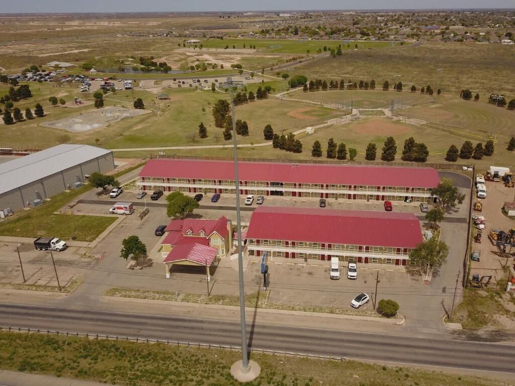 Vista aérea de un complejo de edificios con una estructura de techo rojo, zonas de estacionamiento y campos abiertos circundantes.
